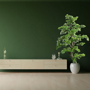 KĂĽnstlicher, detaillierter Bonsai mit weissem Topf vor einer grĂĽnen Wand mit Regal daneben
