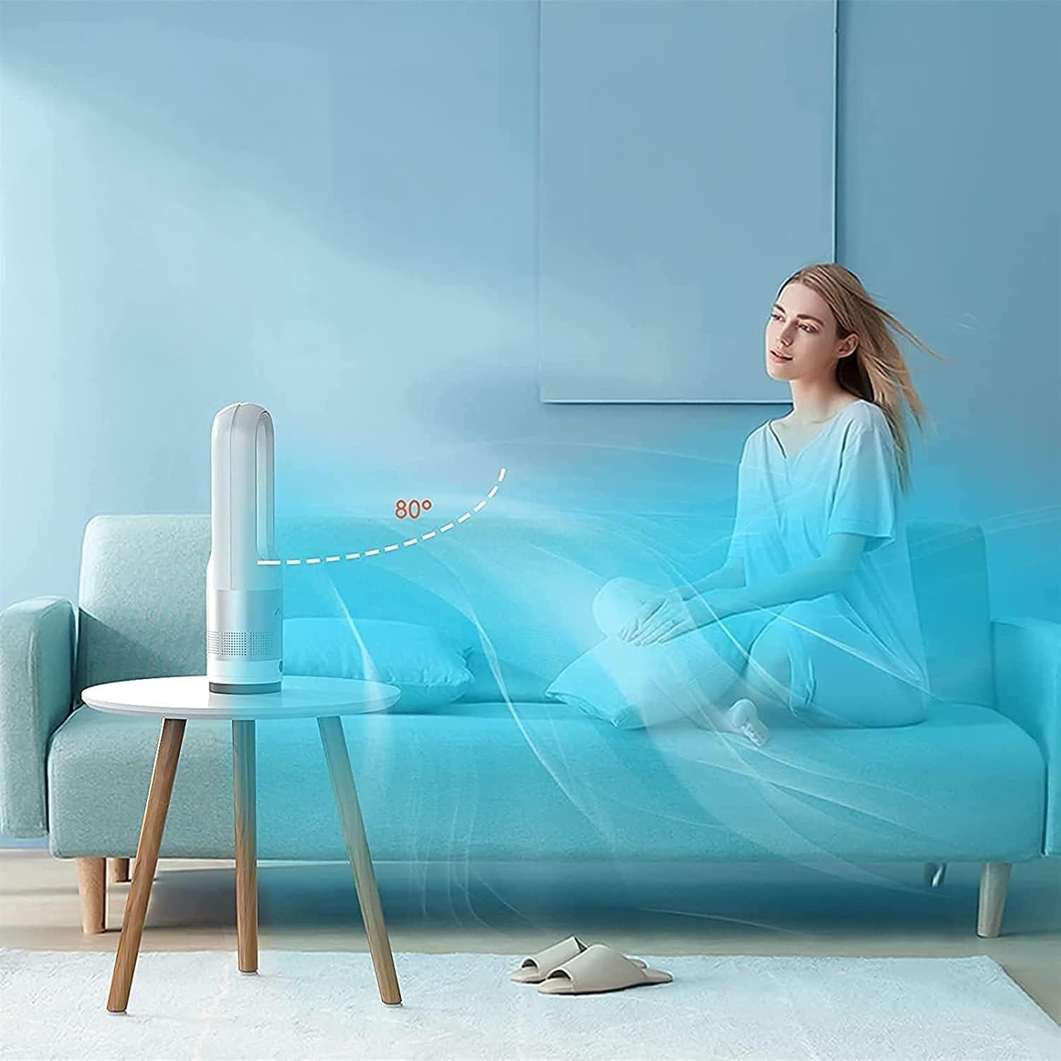 Grauer Turmventilator in Form eines Ovals auf einem kleinen Tisch und einem Sofa mit Person im Hintergrund